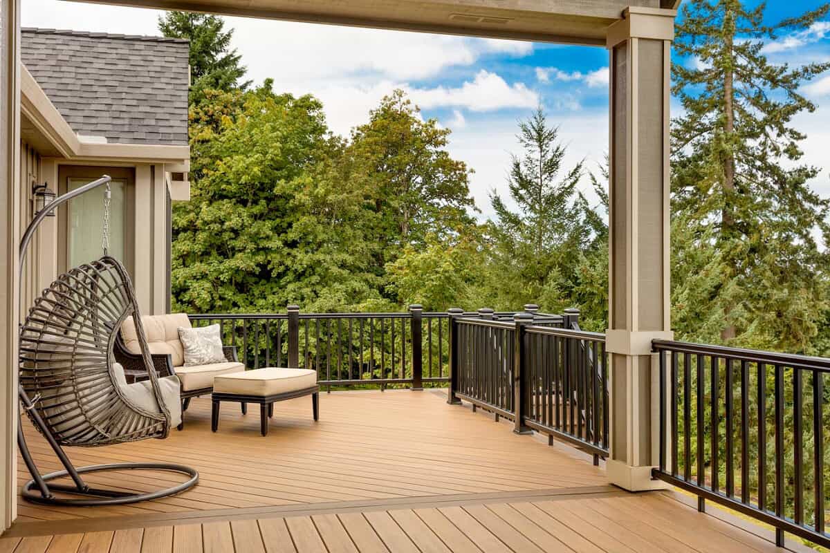 The backyard deck with the black railing, outdoor furniture and tan deck.
